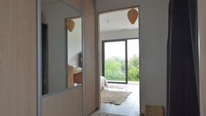 A room with a large mirror, a bed with a view of greenery, and a sliding door leading to a balcony.