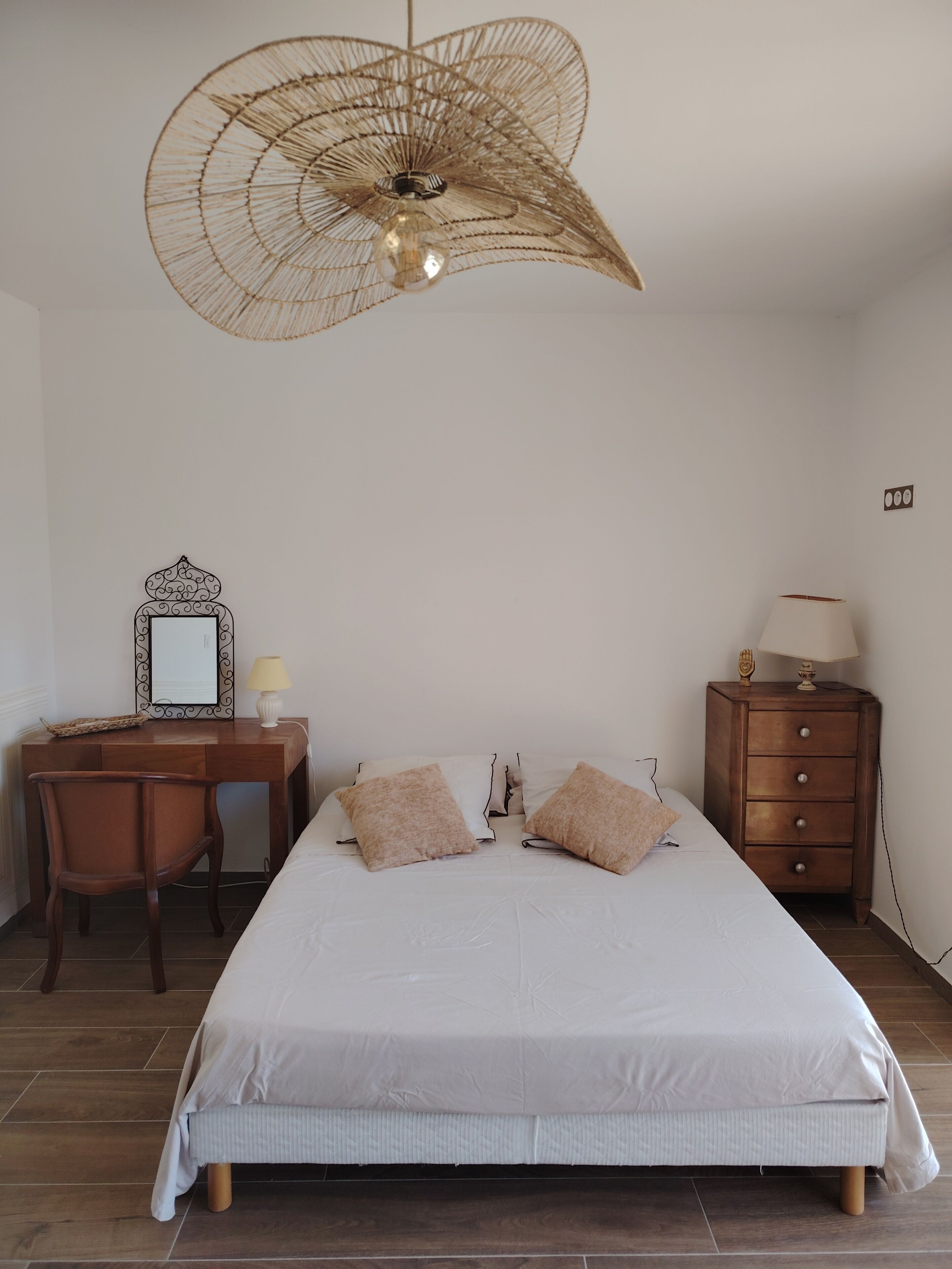 A bedroom with a bed, a desk, a chair, a dresser, and a hanging light fixture.