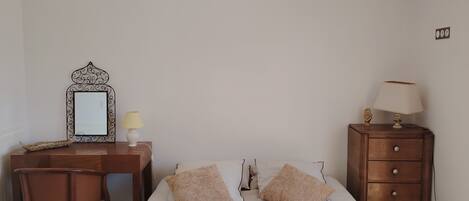 A bedroom with a bed, a desk, a chair, a dresser, and a hanging light fixture.