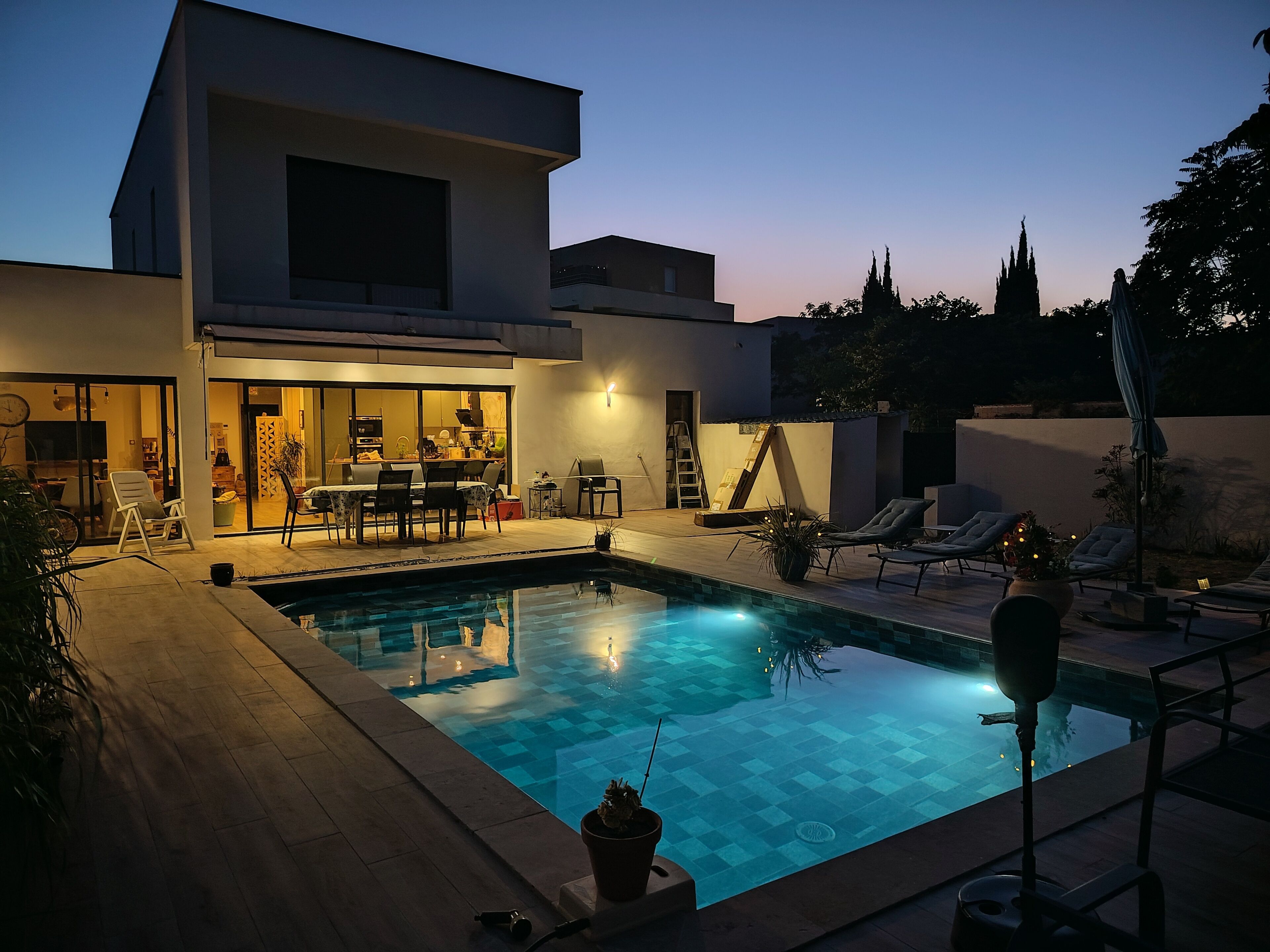 A modern house with a swimming pool, outdoor seating, and a dining area.