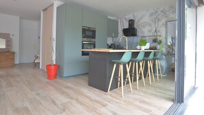 A modern kitchen with a central island, bar stools, and a dining area.