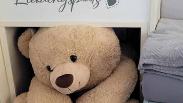 A bed with a white headboard, a bedside table with a radio, and a teddy bear under the bed.