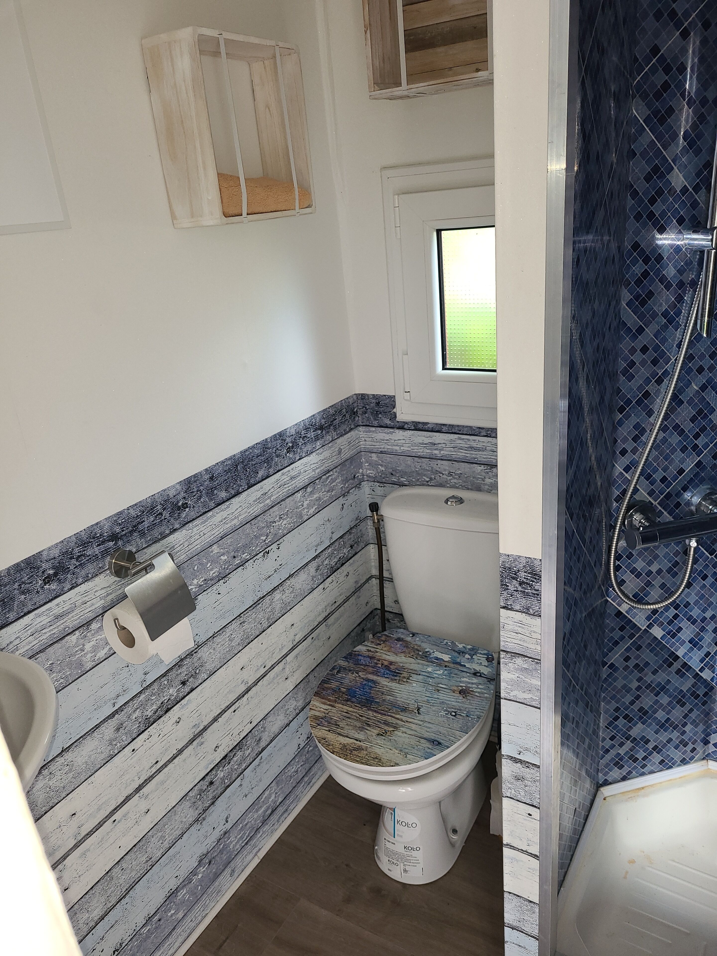 A bathroom with a toilet, a window, and a shower area.