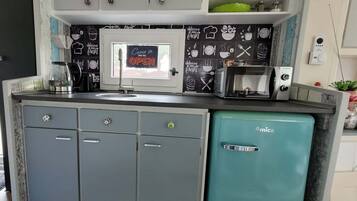 Una cucina compatta con mobili grigi, un mini frigo verde acqua, una macchina da caffè e un forno a microonde.