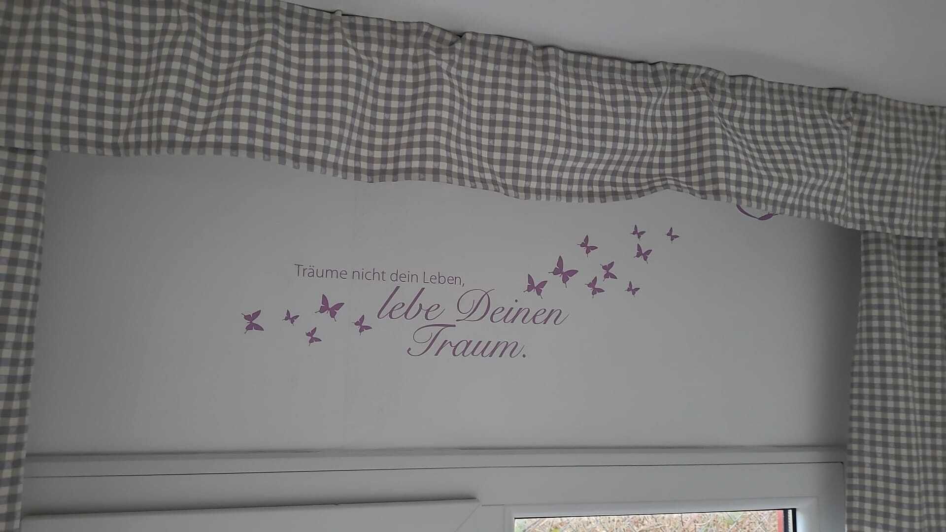 Una pared con un adorno de cortina a cuadros y una frase decorativa con mariposas.