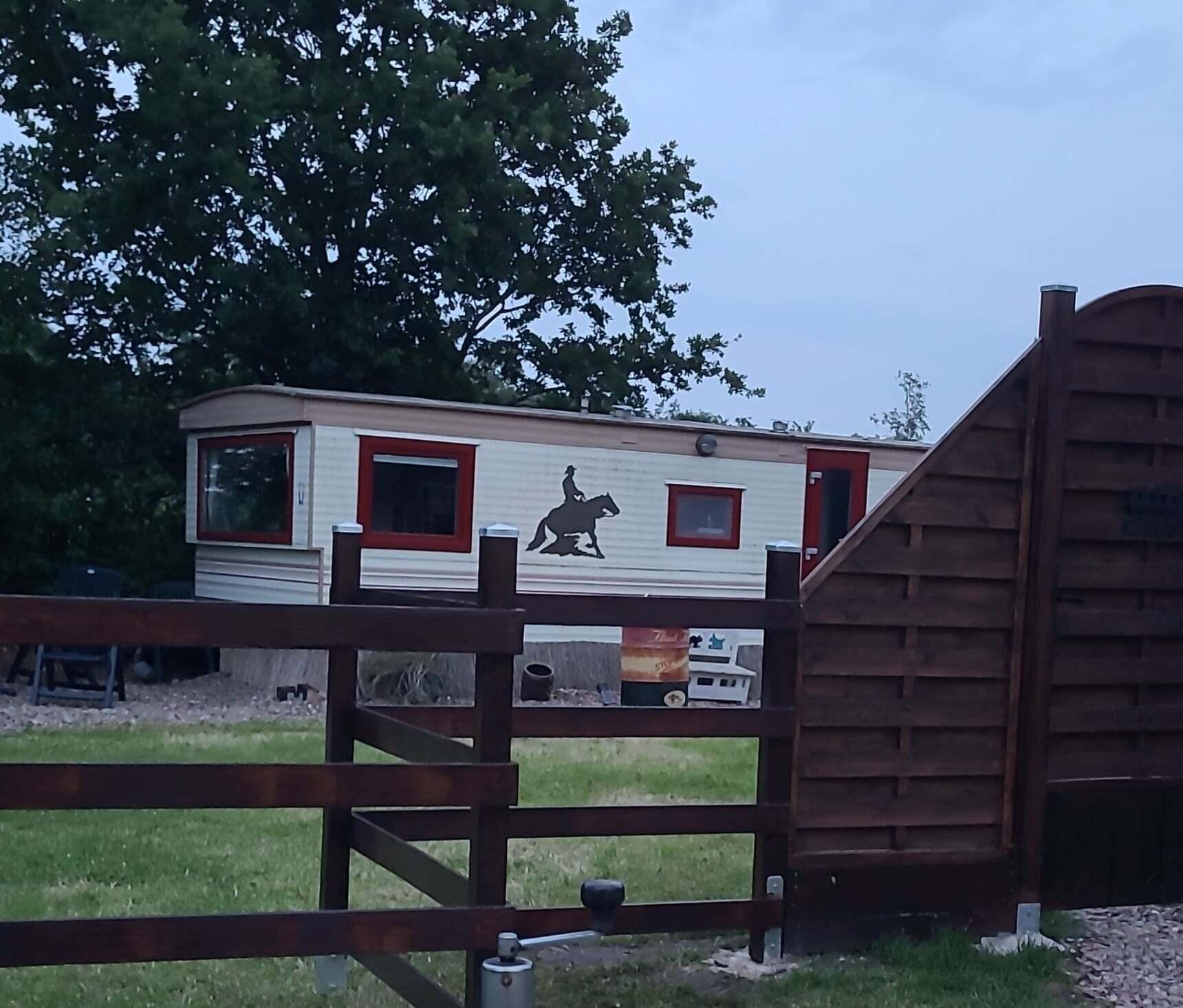 Una casa móvil con un mural de silueta de caballo, una puerta roja y una zona cercada.