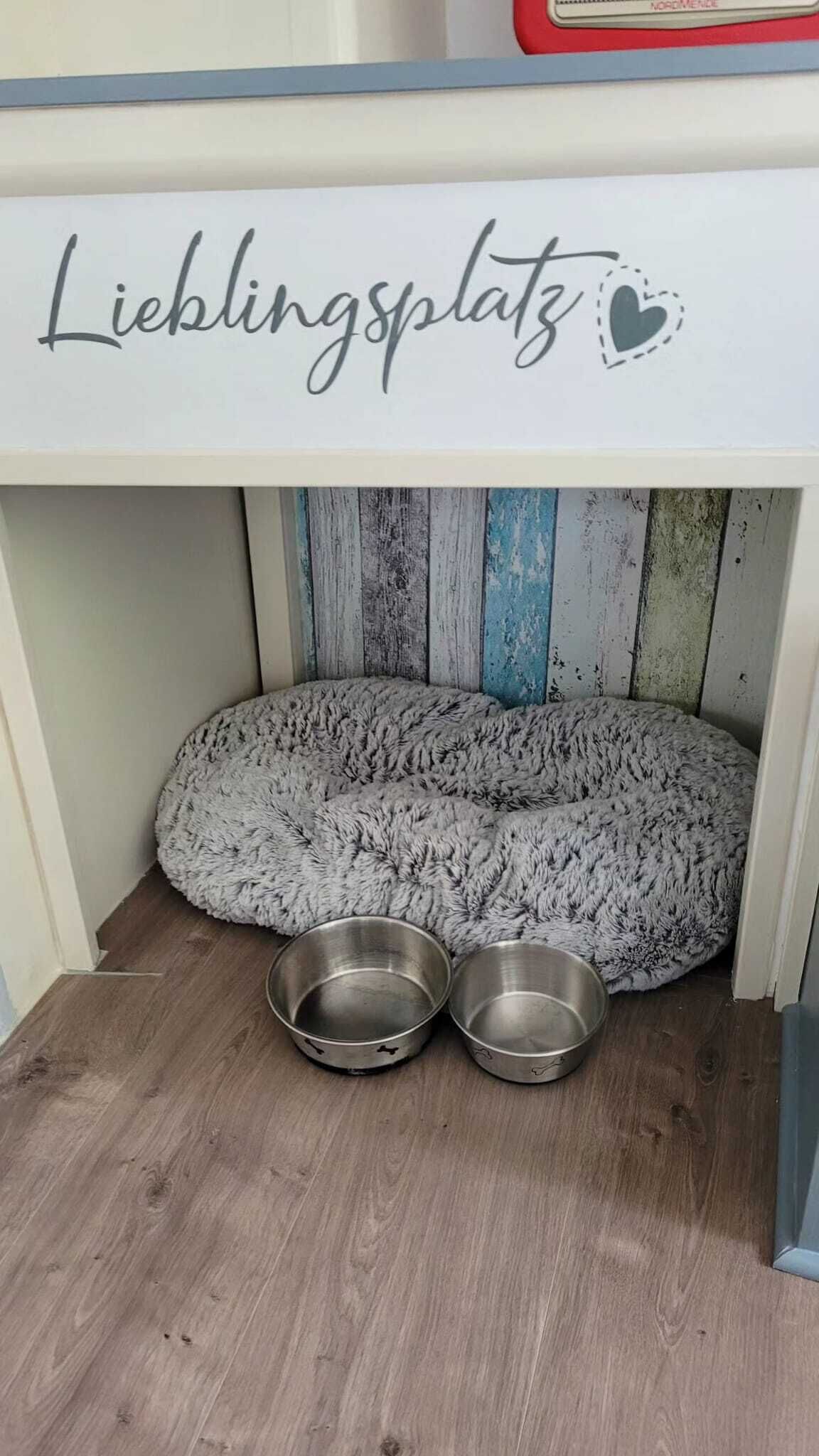 A pet bed labeled "Lieblingsplatz" with two metal bowls underneath.