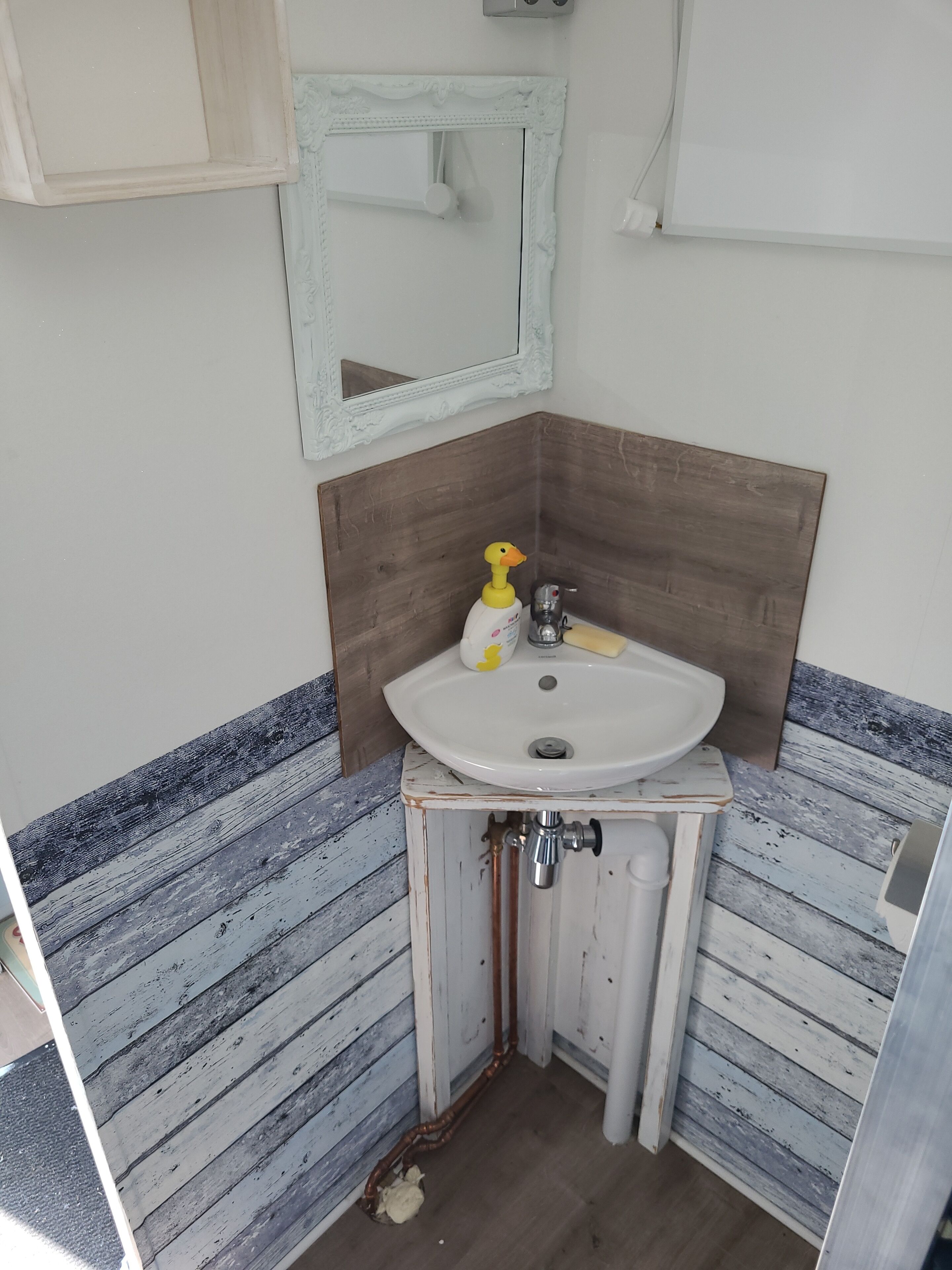 A bathroom with a white sink, wooden vanity, and a mirror with a decorative frame.