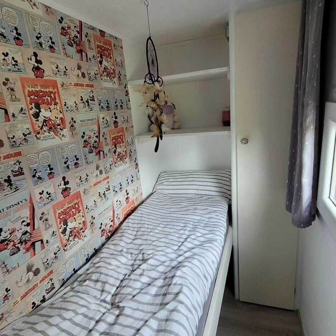 A bedroom with a bed, a wall decorated with Mickey Mouse posters, a dreamcatcher, and a door.