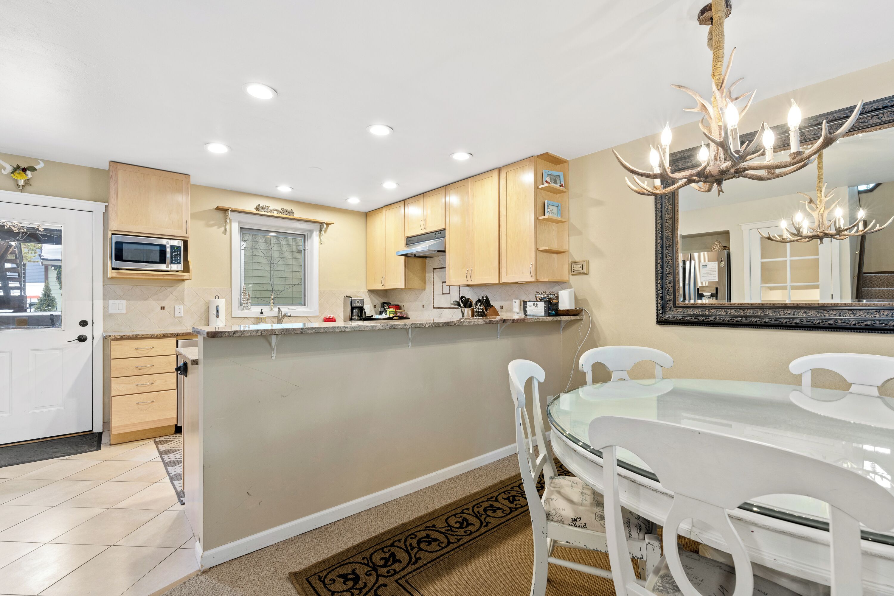 A modern kitchen with wooden cabinets, a microwave, and a dining area with a glass table and white chairs.