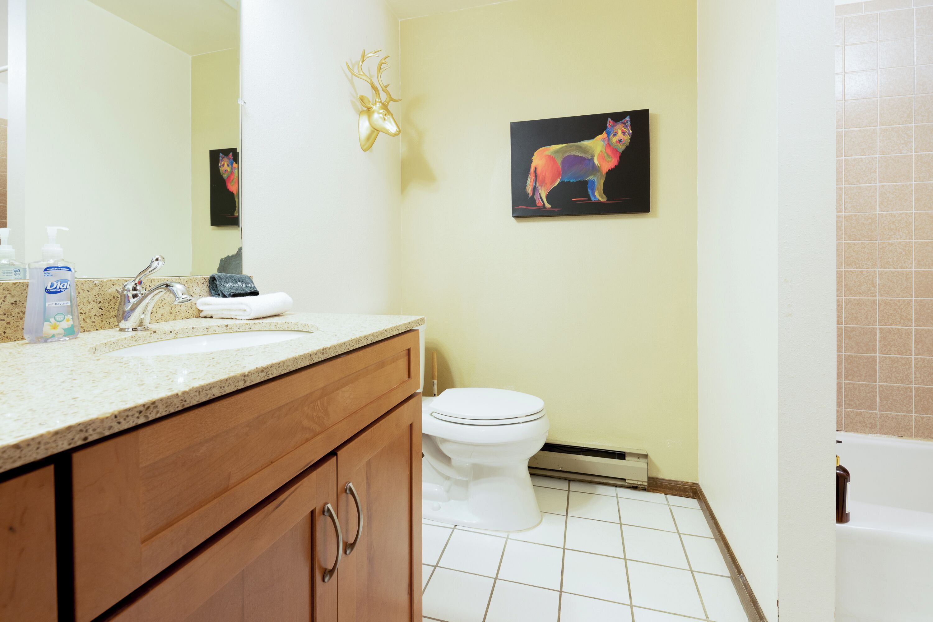 A bathroom with a sink, mirror, toilet, and a wall-mounted deer head decoration.