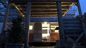 Un espacio al aire libre techado con una estructura de madera, luces colgantes y un vehículo estacionado en su interior.
