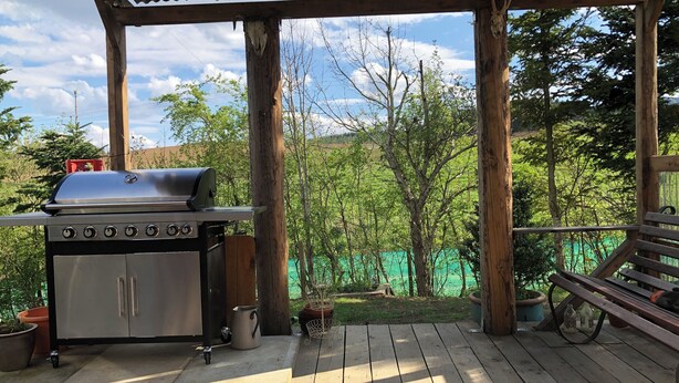 Zona de barbacoa al aire libre con una parrilla, terraza de madera y vegetación circundante.