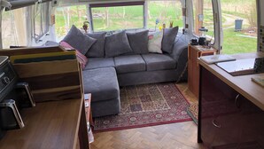 Interior acogedor de una caravana con sofá seccional, zona de cocina y un amplio ventanal con vistas al exterior.