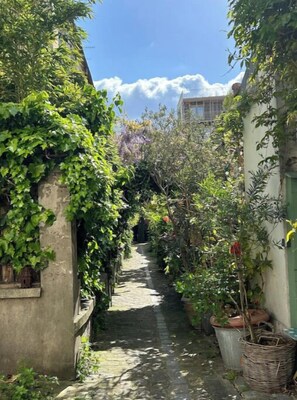 Stroll through a serene, lushly planted alleyway leading to a traditional building with an atmosphere.