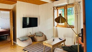 Una habitación acogedora con techo de madera, un televisor de pantalla plana en la pared, una mesita con un florero y un sillón de peluche.