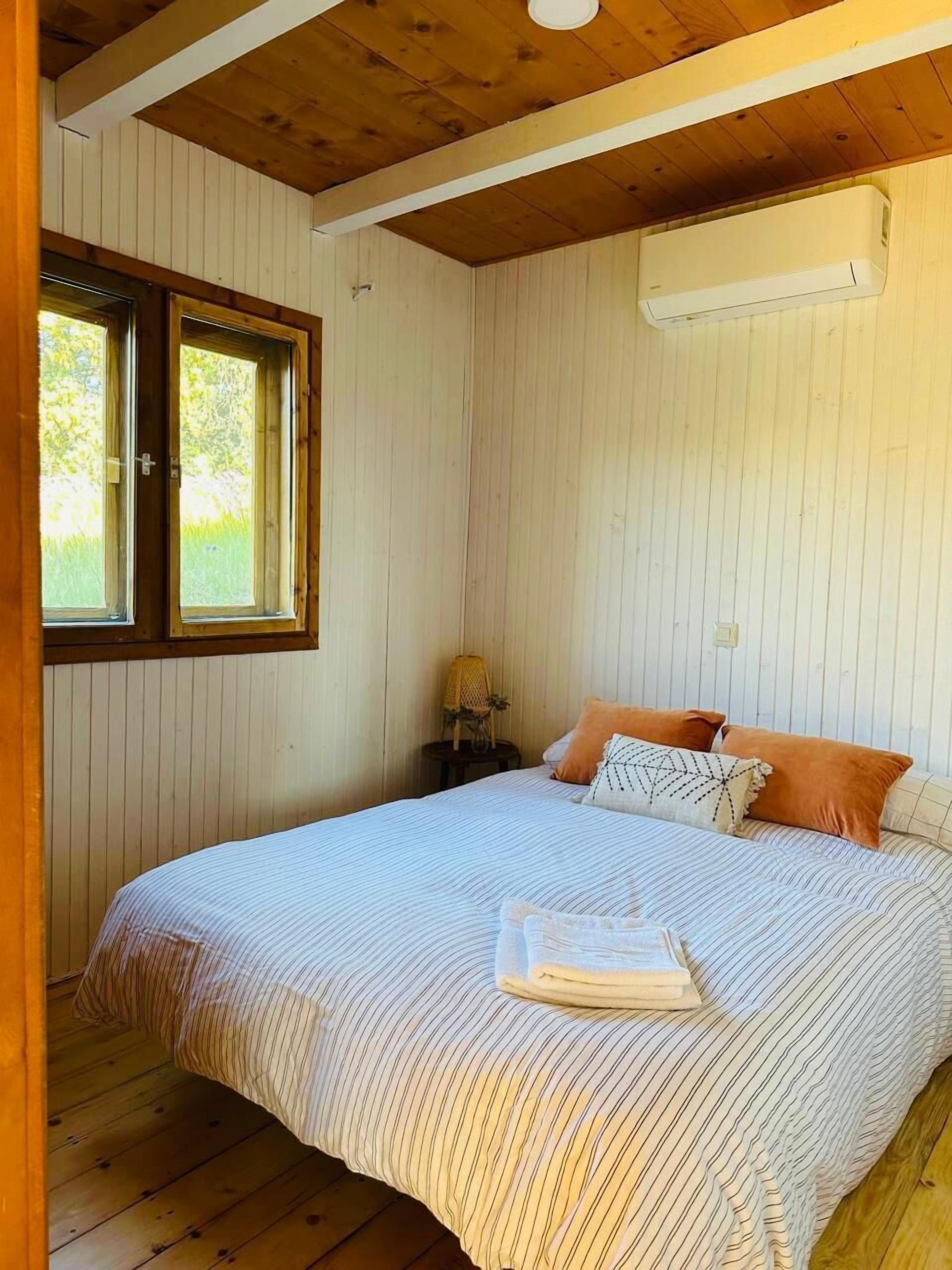 Un dormitorio con una cama grande, paredes de madera, un ventanal y un equipo de aire acondicionado.