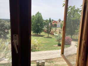A view through a window with a view of a green landscape, a road, and a building with a red roof.