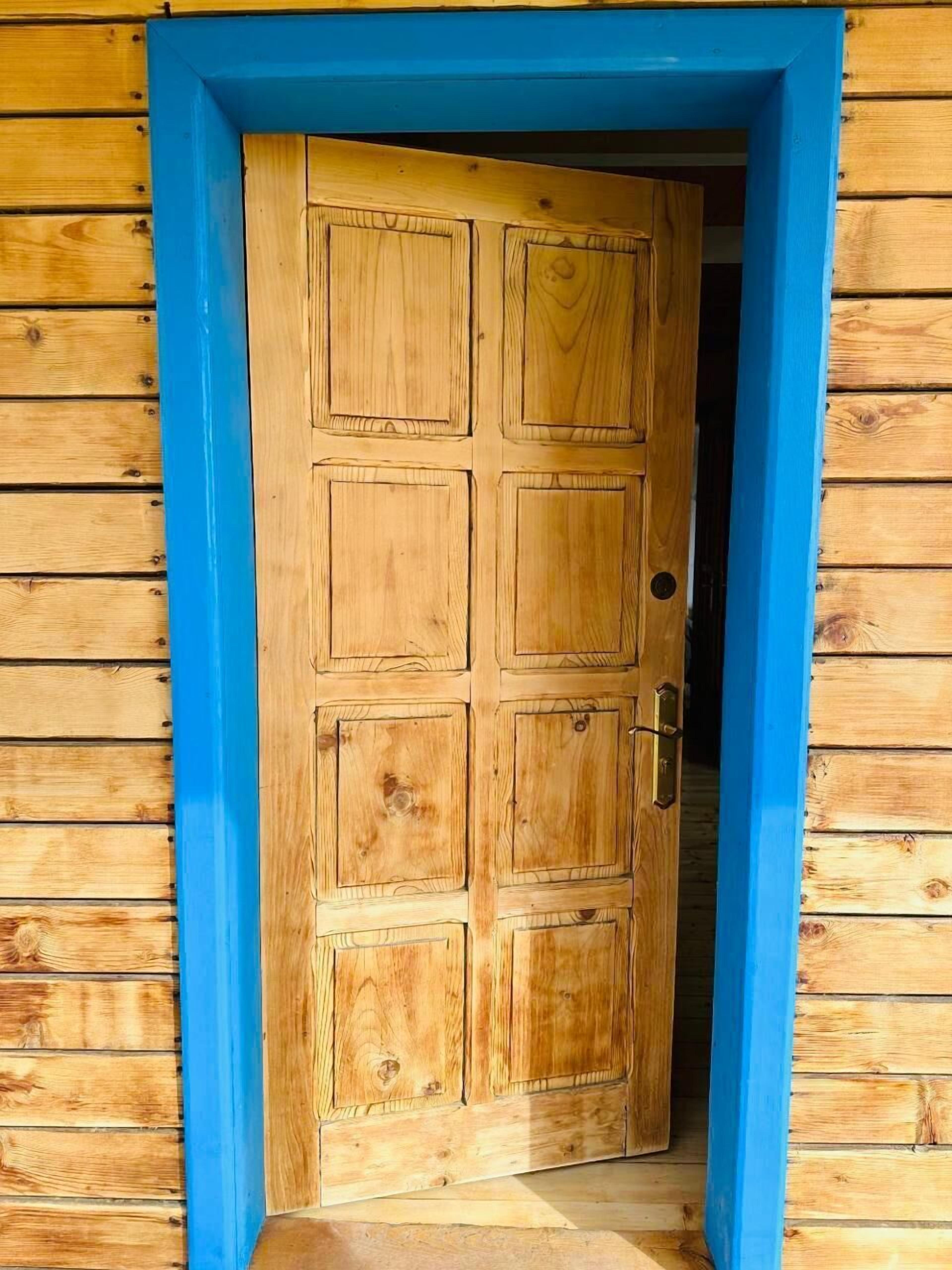 Una puerta de madera con marco azul, que da a un cuarto con paredes de madera.