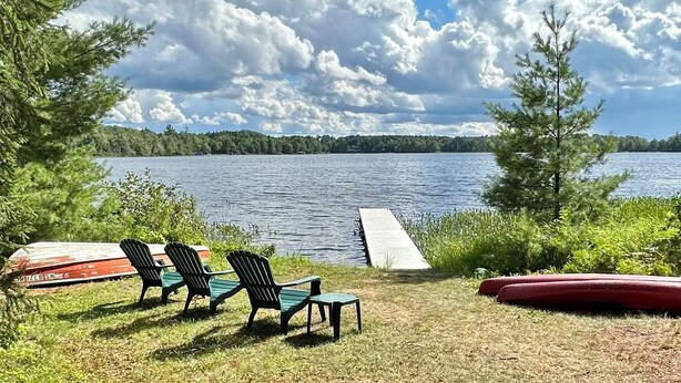 Näkymä järvelle, jossa on laituri, tuoleja ja punainen kanootti.