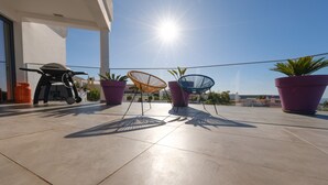 Une terrasse sur le toit avec un barbecue, deux chaises colorées et des plantes en pot.