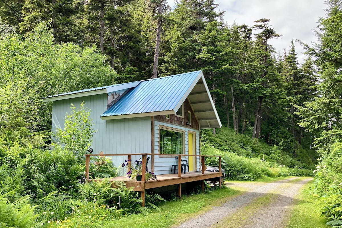 A cabin with a porch, surrounded by dense forest.