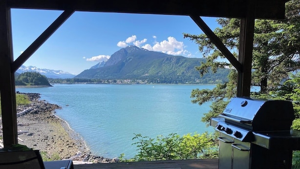 A covered outdoor area with a grill, a chair, and a view of a lake and mountains.