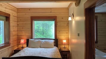 A wooden cabin bedroom with a bed, two bedside lamps, a window, and a door.