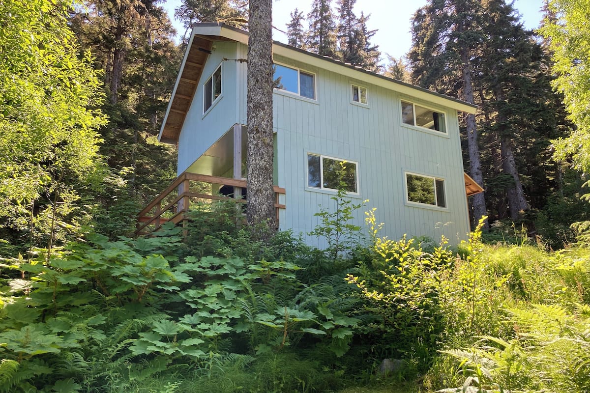 A cabin with a sloped roof, multiple windows, and a wooden staircase leading to a deck.