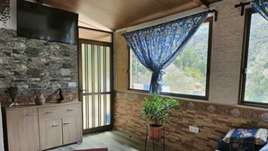 Ein gemütliches Zimmer mit Steinwand, einem Holzkabinett, einer Couch mit gemusterten Kissen, einer Topfpflanze und einem Fenster mit blauen Vorhängen.
