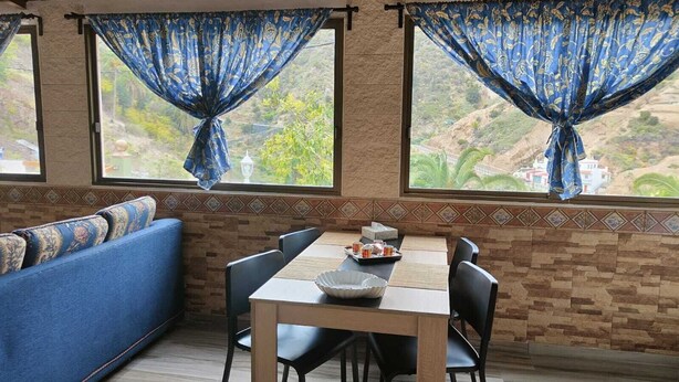 Ein Essbereich mit Tisch und Stühlen, einer Couch und zwei Fenstern mit blauen Vorhängen.