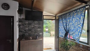 Ein Zimmer mit einer Steinsäule, Holzkästen, einem Flachbildfernseher, einer Topfpflanze und einem Fenster mit gemusterten Vorhängen.
