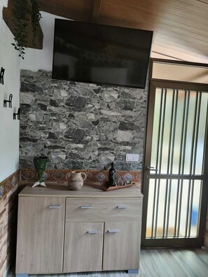 A room with a stone wall, a flat-screen TV mounted above a wooden cabinet, and a sliding glass door with a view. - Casa Vacacional Lupe (CN)