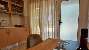 A dining area with a wooden table, chairs, a wine bottle, and a view through a glass door. - Honeywell Comfort Stay (Markopoulo Mesogaias)