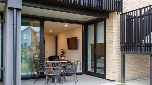 A modern outdoor patio with a round table and four chairs, a potted plant, and a TV mounted on the wall. - Apartment with style (Wanaka)