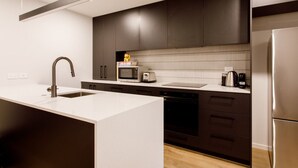 A modern kitchen with a large island, dark cabinetry, a microwave, toaster, and a refrigerator. - Apartment with style (Wanaka)