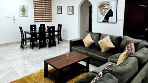 A modern living room with a dark green sofa, a wooden coffee table, and a dining area with a black table and chairs. - Gorgeous Quiet & Comfy Close to Highway (Adentan)