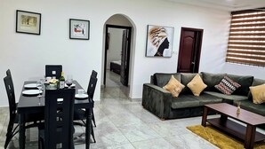 A modern living room with a dining area, featuring a sofa, coffee table, and a dining table set with chairs. - Gorgeous Quiet & Comfy Close to Highway (Adentan)