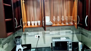 A kitchen with wooden cabinets, a microwave, a toaster, a blender, and a shelf with cups and glasses. - Gorgeous Quiet & Comfy Close to Highway (Adentan)