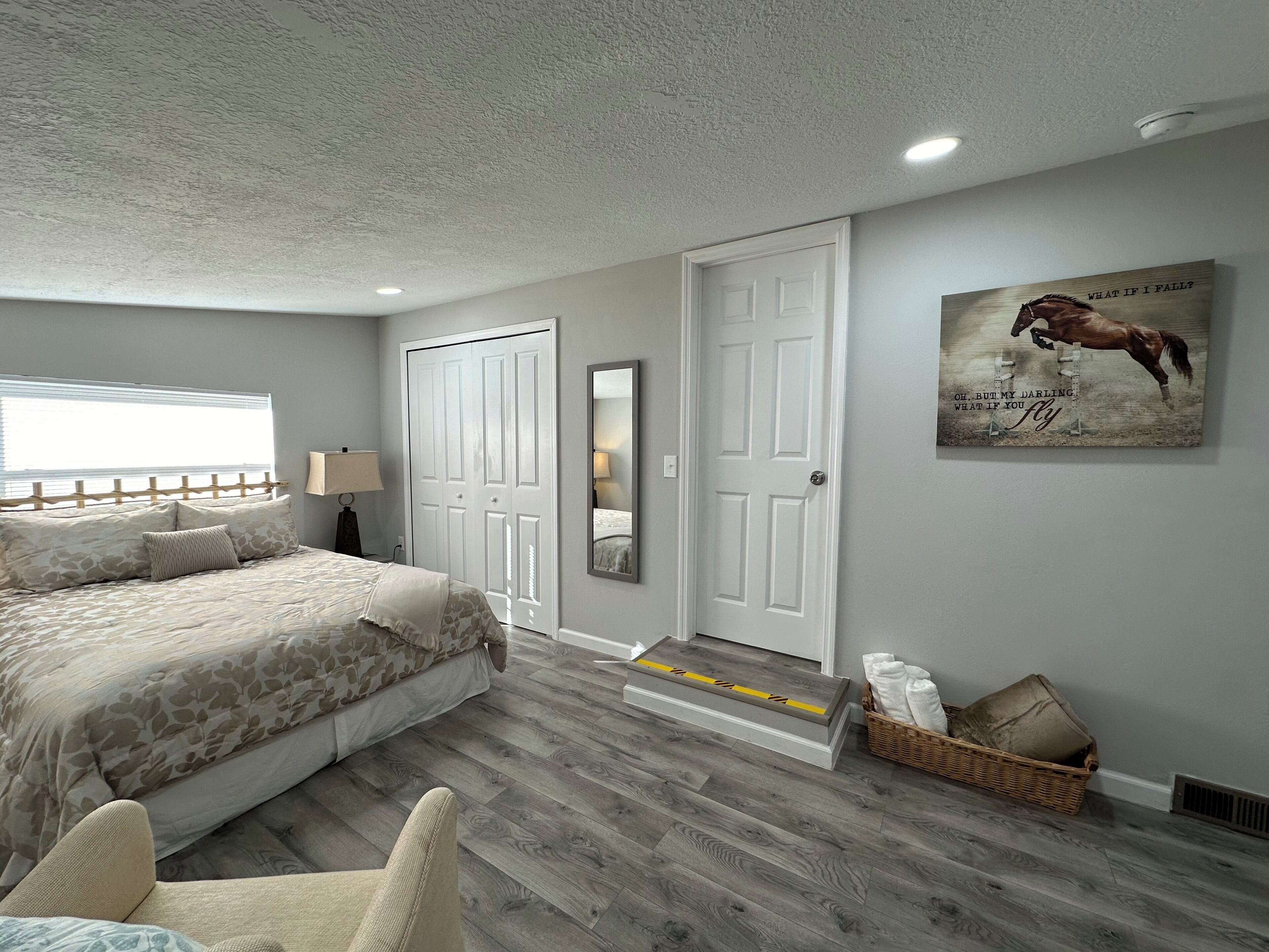 A bedroom with a bed, a chair, a door, a mirror, and a wall with a poster.