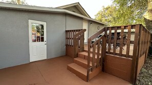 A house with a grey exterior, a white door, and a wooden staircase leading to a covered patio area.