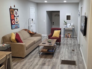 A living room with a sofa, armchair, coffee table, and a wall-mounted artwork. - Fully Equipped Cottage, Right Next to Lake Weir (Ocklawaha)