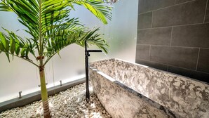 A modern bathroom with a stone bathtub, a palm tree, and a pebble-lined floor. - La Ola Perfecta - Las Golondrinas Hacienda Pinilla (Hacienda Pinilla)
