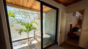 A modern interior with a sliding glass door leading to a patio area with a palm tree and a stone bath. - La Ola Perfecta - Las Golondrinas Hacienda Pinilla (Hacienda Pinilla)