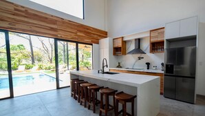A modern kitchen with a large island, bar stools, a built-in oven, and a refrigerator. - La Ola Perfecta - Las Golondrinas Hacienda Pinilla (Hacienda Pinilla)