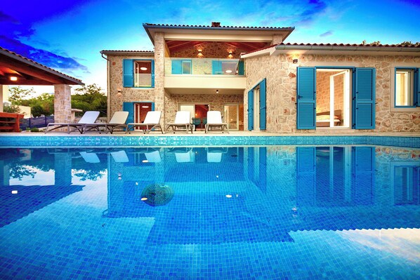 A two-story stone building with a swimming pool, outdoor seating, and a balcony.