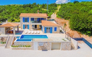 Ein zweistöckiges Steinhaus mit Swimmingpool, überdachter Terrasse und einer Treppe, die zum oberen Stockwerk führt.