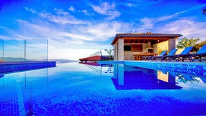 Un espace piscine offrant une vue dégagée sur la piscine, des chaises longues et un bâtiment doté d’un toit en tuiles.