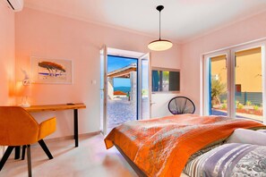A bedroom with a bed, a desk, and a chair. There is a door leading to an outdoor area.