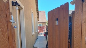 Une ruelle étroite, bordée de chaque côté par des clôtures en bois, qui mène à un bâtiment à la façade beige et au toit rouge.